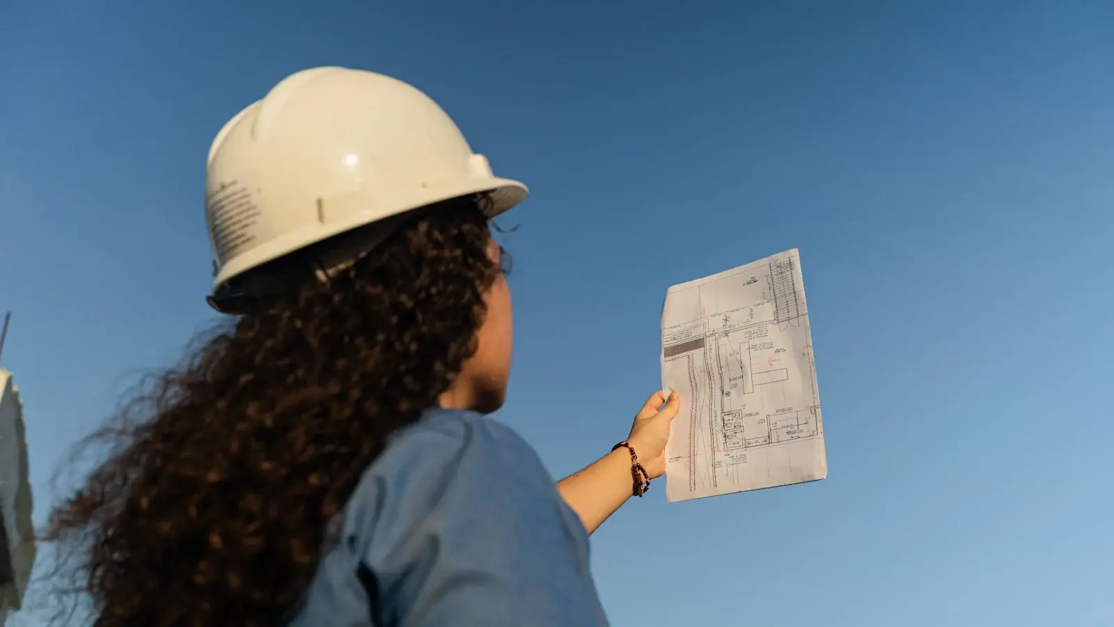 Ingeniera con casco de seguridad revisando un plano en obra